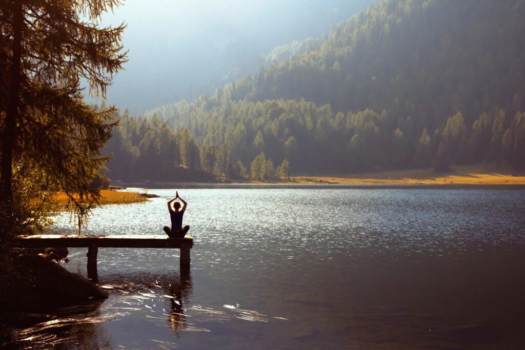 Woman meditating on the end of a pier over a mountain lake